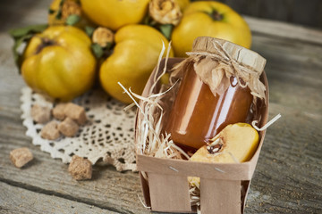 jar of jam in basket and quinces with leaves on wooden rustic background