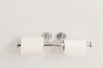 horizontal image of two rolls of toilet paper hanging on a double stainless steel toilet paper holder on a white wall.