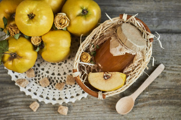 jar of jam in basket and quinces with leaves on wooden rustic background