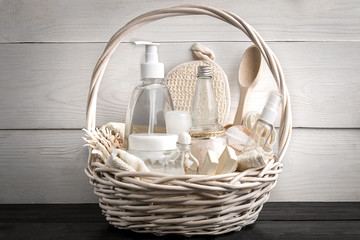 Composition of cosmetic bottles and soap in basket, on white wooden background