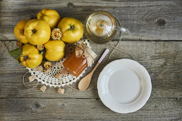empty plate with jar of jam and quinces on rustic wooden background