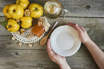masculine hands holding empty plate with jar of jam and quinces on rustic wooden background