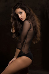 Fototapeta na wymiar Attractive brunette model with bright makeup in black lingerie posing near dark wall
