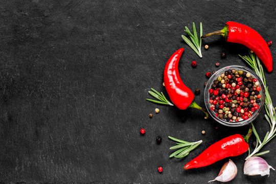 Red hot chili peppeprs and peppercorns with rosemary and garlic on black stone background