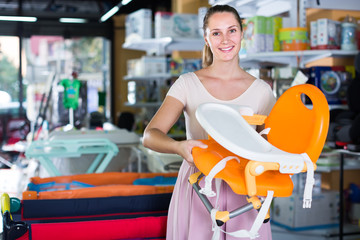 beautiful pregnant woman choosing chair for feeding baby at infant shop