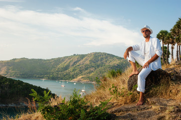 Naklejka na ściany i meble man sitting on a rock and looking at the sunset of Phuket