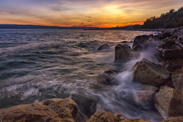 Obraz premium Sunset over the sea with splash waves on the rocks