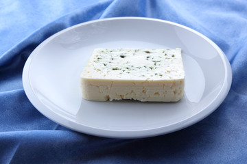Cheese with mildew on a white plate, goat cheese on a blue background, cheese on a white plate on a blue napkin, cheese in a minimalist style, retro style