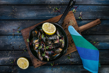 Delicious mussels. Serving on a hot frying pan with herbs spices and lemon on a colored wooden background. Top view