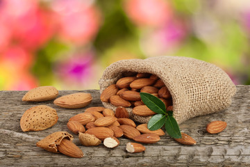 Almonds with leaf in bag from sacking on a wooden table with blurred garden background