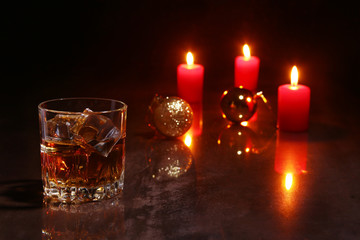 christmas decoration. glass of cognac or whiskey, red candles and colorful ball on a wooden background.