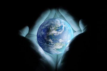 Men's hands holding the planet earth rotated the continents of North and South America with a blue glow on a black background.