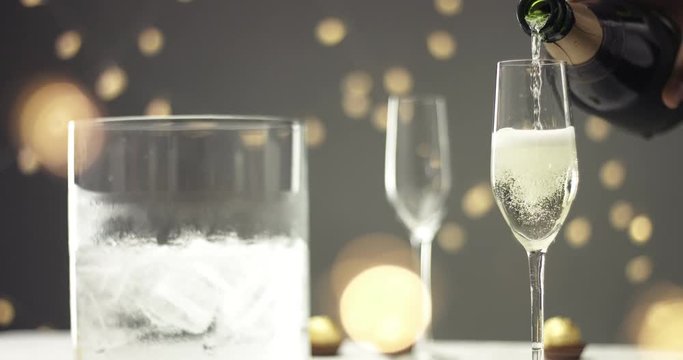 Close up video of pouring sparkling wine into a chilled glass on gray backround with blurred lights