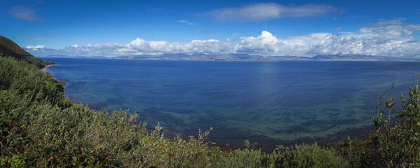 Fototapeta na wymiar Vue panoramique dans le comté de l'anneau du Kerry. Un bras de mer, avec au fond des collines ensoleillées et ruban de nuages. Au premier plan la plage et de la verdure