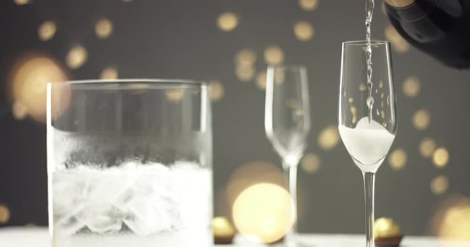 Close up video of pouring sparkling wine into a chilled glass on gray backround with blurred lights
