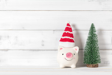 Piggy bank and santa claus hat with christmas tree on white wood over white rustic background with copy space for text