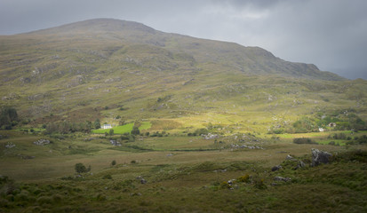 Fototapeta na wymiar Vue panoramique du parc national de killarney, en Irlande; Au fond des collines et une maison isolée baignées de soleil. Au premier plan des rochers et de la verdure