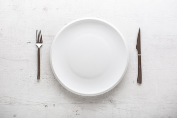 Top of view empty plate with fork and knife on white concrete background