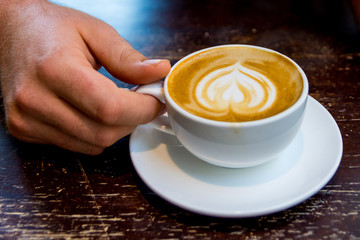 Man Holding Latte Art Cappuccino Across Wooden Table