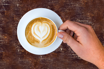 Guy Holding White Mug Latte Art From Above on Wooden Table in Coffee Shop