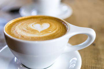 Latte Heart Art White Mug at Coffee Shop Cup in Background Blurred Wooden Table