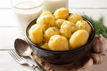 Boiled potatoes with dill in bowl on white wooden background.
