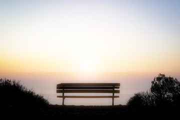 Empty bench overlooking the colorful light of sunset over the horizon of the Pacific Ocean off the...