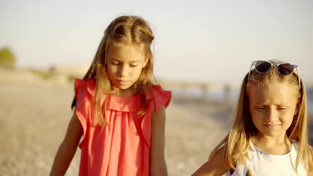 two cute girls sisters walking along the seashore holding hands each other