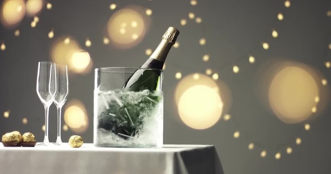 Panning on ice bucket with a bottle of champagne, flute glasses on a table covered with white tablecloth with festive lights and flares