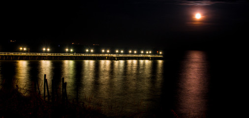 Fototapeta na wymiar Widok na molo nocą w Gdyni Orłowo blisko klifu, księżyc odbija się w spokojnym morzu bałtyckim