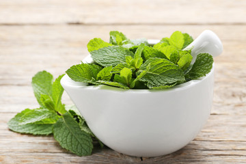 Fresh mint leafs in mortar on grey wooden table