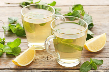 Cup of tea with mint leafs and lemons on wooden table
