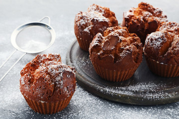 Tasty muffins with cutting board and sieve on grey wooden table