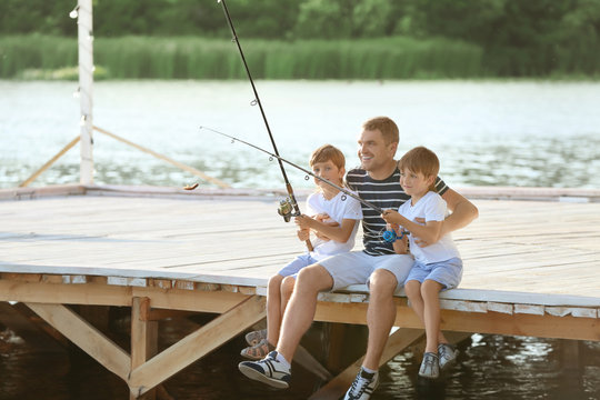 Father with sons fishing from pier on river