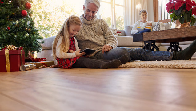 Senior man with granddaughter using digital tablet at home