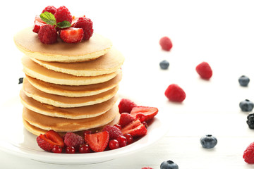 Tasty pancakes with berries on white wooden table