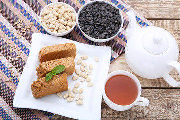 Tasty slices of halva in white plate with cup of tea on wooden table