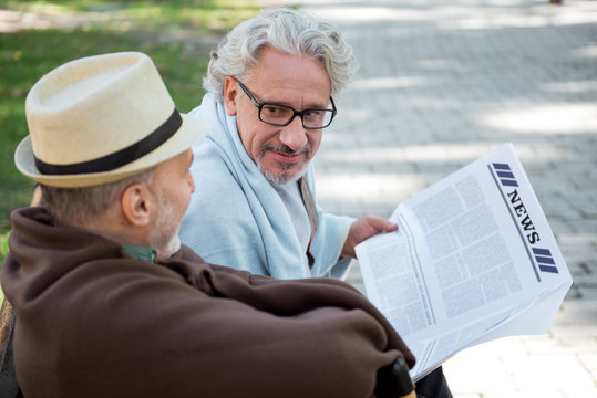 Joyful senior male friends reading newspaper