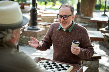 Cheerful mature male pensioners entertaining with draughts in park
