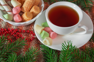 Warm Christmas background. Cup of tea, sweets, Christmas beads and sprigs of fir on knitted background. Studio is a place for text.