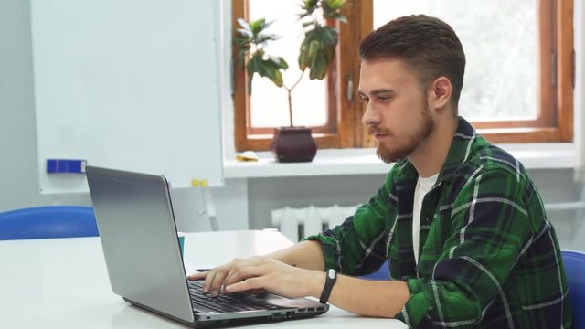A young man is sitting at a computer in an educational institution