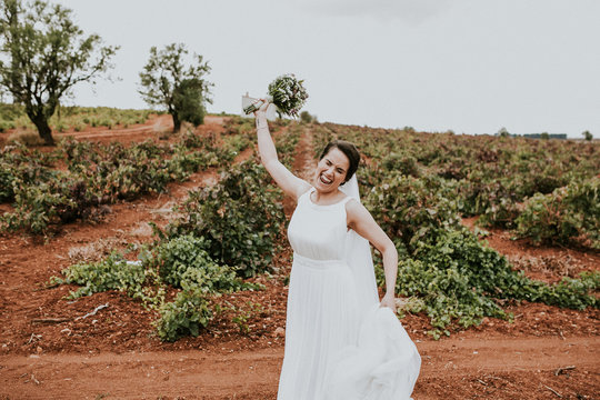 .Young and beautiful bride taking pictures on their wedding day in a beautiful field surrounded by vineyards. Celebrating her marriage. Lifestyle photography.