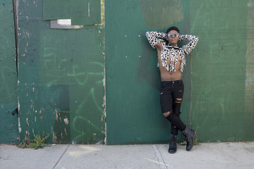 Young man in spotted and torn shirt standing against wooden wall 