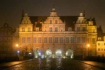 Cobblestone street and historic Green Gate in Old Town of Gdansk in the fog at night. Poland.