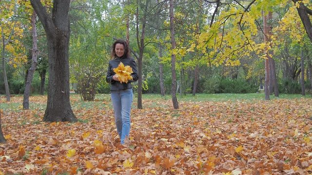 Happy woman with yellow leaves in hands walking in autumn park.