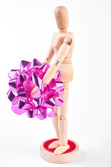 Wooden dummy holding pink bow. Human wooden mannequin with gift bow isolated on white background, side profile. Holidays and celebrations concept.