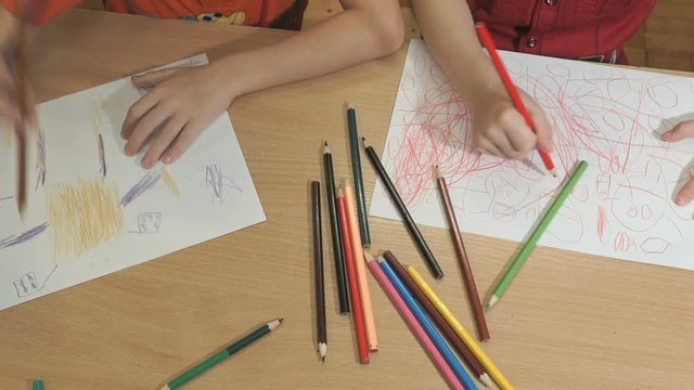 Close-up of hands of unidentified little boys drawing pictures using multicolored pencils in kindergarten