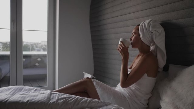 Woman with coffee on a bed in a hotel room