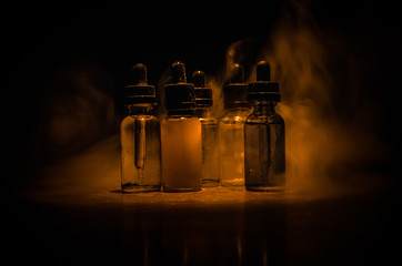 Vape concept. Smoke clouds and vape liquid bottles on dark background. Light effects. Useful as...