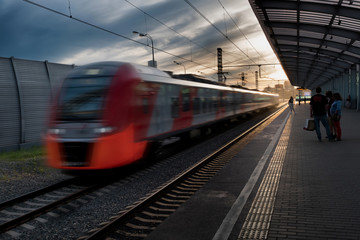 High-speed beautiful red modern train in motion at the railway station at sunset in Europe. Blur effect. Industrial scene with a passenger train on the railway on the sunset